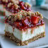 A plated Strawberry Cheesecake Bar reveals creamy vanilla filling and juicy strawberries over a buttery graham cracker crust.