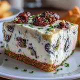 Savory Kalamata cheesecake appetizer with creamy filling, olive-studded surface, and crisp cracker on white plate.