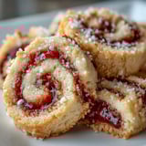 Buttery shortbread cookies with vibrant raspberry swirls, lightly dusted with sugar on a white plate.
