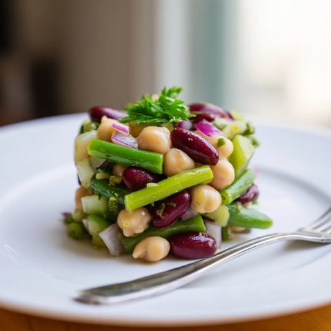Three-Bean Salad with crisp red onion and celery tossed in a zesty apple cider vinaigrette, served chilled for a refreshing side.