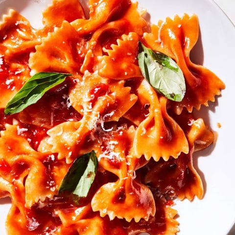 Steamed bowtie pasta is coated in a creamy, vibrant tomato basil sauce, garnished with fresh basil leaves and Parmesan cheese.