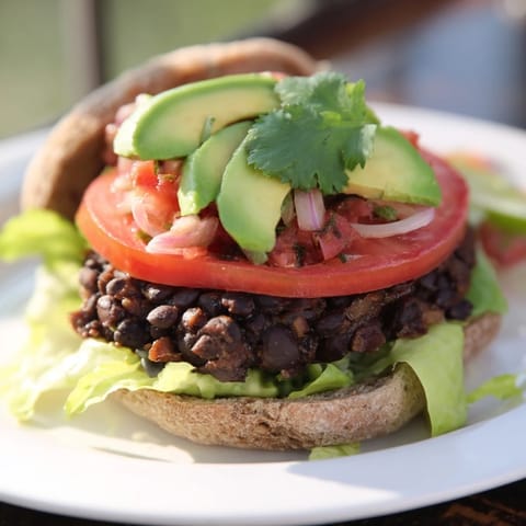 Golden-brown Zesty Weeknight Black Bean Burgers ready to eat, served with lime wedges and toppings.