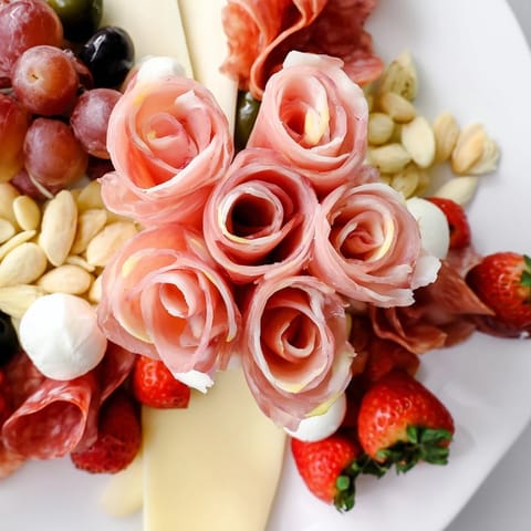 Prosciutto rose bouquet board boasts savory prosciutto roses, creamy cheeses, and colorful fruit for serving.