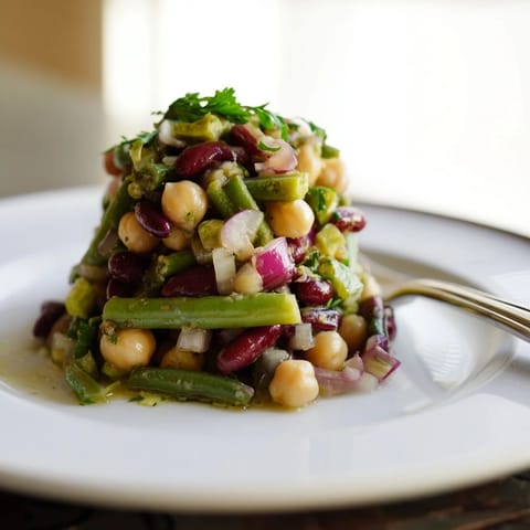 Vibrant bowl of Three-Bean Salad featuring green beans, kidney beans, and chickpeas, glistening with tangy dressing and fresh parsley.