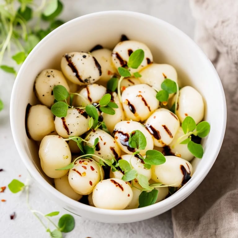 A small bowl full of mozzarella pearls, a vegetarian Italian recipe enhanced with basil and balsamic glaze.