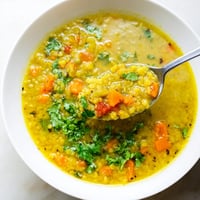 A steaming bowl of homemade mung bean soup with tender beans and diced carrots, garnished with fresh cilantro.  